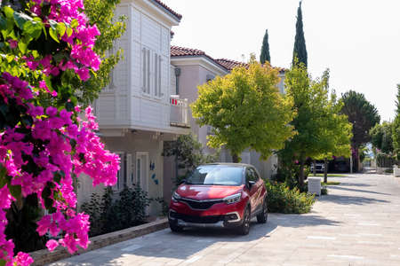 red car is parked near a private house, a lot of greenery and flowersの写真素材