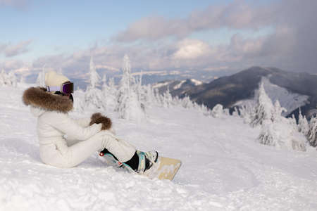 winter, leisure, sport and people concept - Young beautiful female snowboarder resting on ski slope, she's looking away and smilingの写真素材