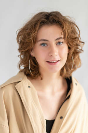 Portrait of Caucasian woman with smoothly tucked hair and natural makeup in raincoat with. The lady is holding the collar of her cloak, posing against a white background and looking at camera. photoの写真素材