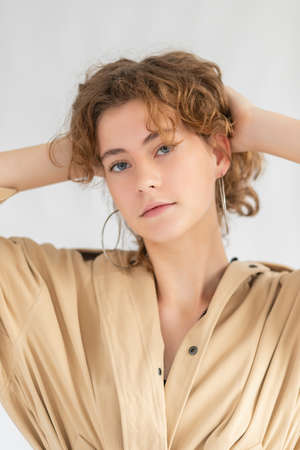 Portrait of Caucasian woman with smoothly tucked hair and natural makeup in raincoat with. The lady is holding the collar of her cloak, posing against a white background and looking at camera. photoの写真素材