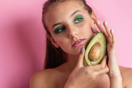 Close up view of gorgeous ginger woman with avocado. Studio shot of excited caucasian girl with healthy food isolated on pink background.の写真素材