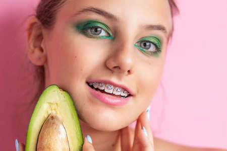 Close up view of gorgeous ginger woman with avocado. Studio shot of excited caucasian girl with healthy food isolated on pink background. girl with bracesの写真素材