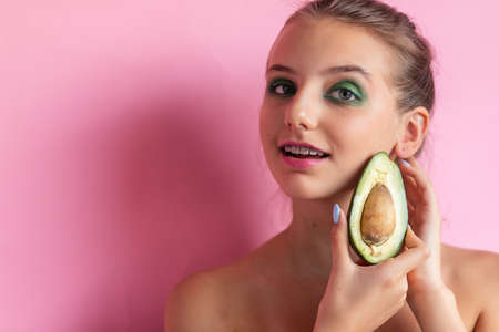 Close up view of gorgeous ginger woman with avocado. Studio shot of excited caucasian girl with healthy food isolated on pink background. girl with bracesの写真素材