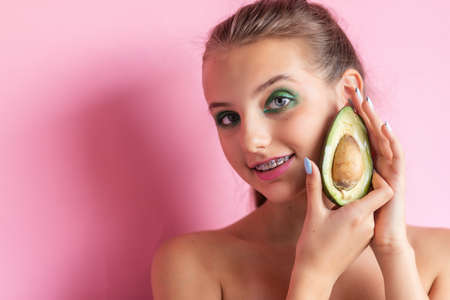 Close up view of gorgeous ginger woman with avocado. Studio shot of excited caucasian girl with healthy food isolated on pink background. girl with bracesの写真素材