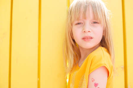 Laughing portrait of a cute girl, a child hears a joke on a yellow studio backgroundの写真素材