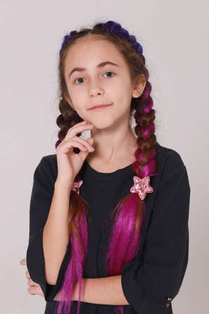 Cute girl in black dress and long braids on light gray background, smiling girlの写真素材