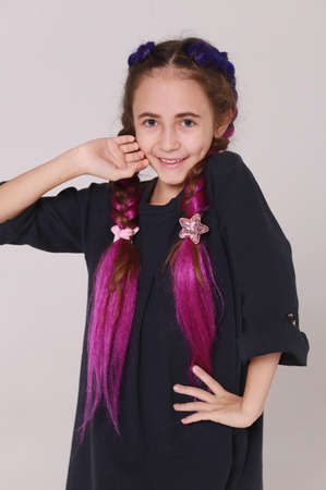 Cute girl in black dress and long braids on light gray background, smiling girlの写真素材