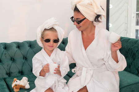 Mother with child doing beauty treatment together. Happy family mother and child daughter in towel and bathrobe are sitting on the couch. beauty salon concept, wellness spa, long banner formatの写真素材