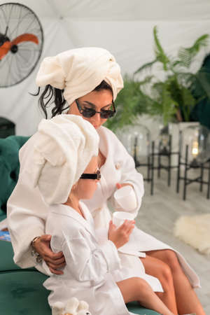 Mother with child doing beauty treatment together. Happy family mother and child daughter in towel and bathrobe are sitting on the couch. beauty salon concept, wellness spa, long banner formatの写真素材