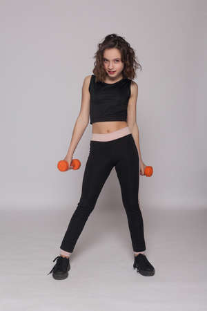 Brunette girl in a white T-shirt and coral leggings posing with dumbbells in her hands in front of a white wallの写真素材