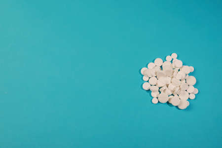 White medical pills, tablets and capsules from pharmacy on turquoise background. Macro top down view...
