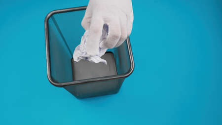 Hand throwing crumpled paper into the office trash isolated on blue backgroundの写真素材