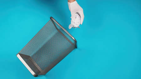 Hand trowing a paper into a wastebasket on blue backgroundの写真素材