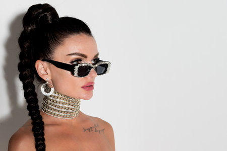 Exuding sophistication and style, a woman with sunglasses and a flowing ponytail hair strikes a glamorous pose in a close-up studio portrait, her allure undeniableの写真素材