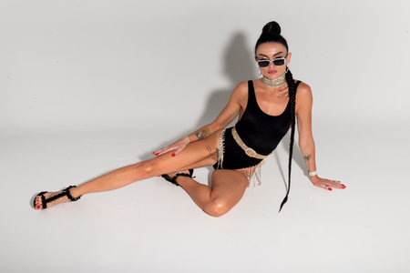 With grace and poise, a slender model showcases her chic black lingerie and taut physique as she poses on the studio floor, her long ponytail cascading elegantly behind herの写真素材