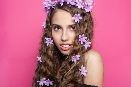 Elegant girl showcases her curly locks adorned with delicate purple flowers, exuding a charming and romantic aura in a floral arrangementの写真素材