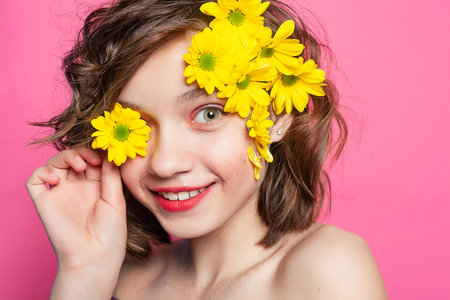 Captivating image of a girl gracefully holding a yellow flower, adding a touch of mystery against a pastel pink background. Ideal for spring-themed promotions.の写真素材