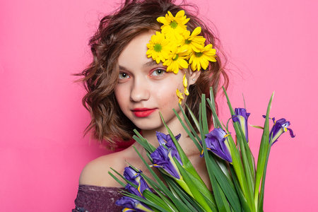 Whimsical photograph of a woman playfully hiding behind a vibrant yellow blossom on a delicate pink background. Great for expressing spontaneity and joy.の写真素材