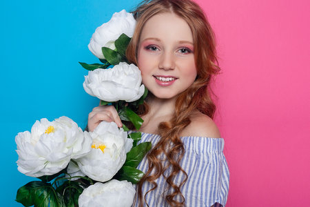 Adorable young girl, surrounded by delicate white flowers, her face hidden in a playful gesture against a soft pink backdrop. Perfect for sweet and innocent concepts.の写真素材