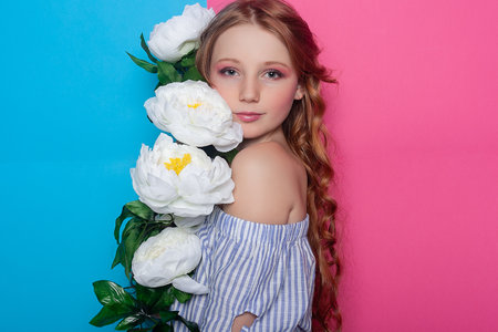 Enchanting photograph of a little girl amidst white flowers, her face partially concealed, evoking a sense of wonder against the pastel pink background. Perfect for dreamy concepts.の写真素材