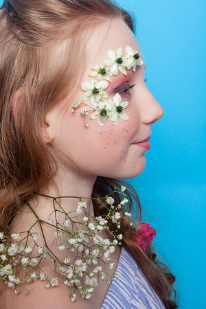 Captivating image of a girl with daisies on her face, set against a vivid blue background, adding a pop of color and whimsy to any project.の写真素材