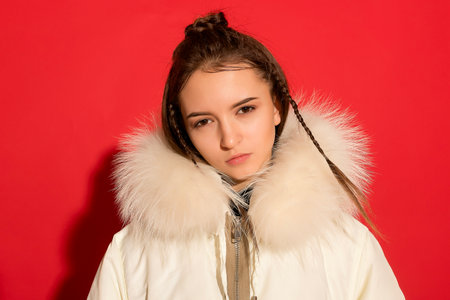 Fashion-forward sophistication! A young girl showcases her style against a striking red backdrop in the studio, adding elegance with a white jacket.の写真素材