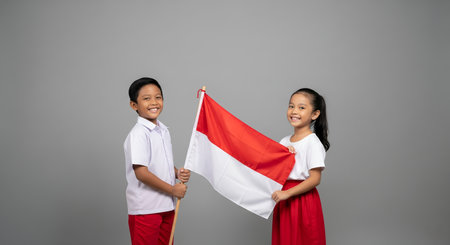 A boy and a girl, dressed in red and white, joyfully hold the Indonesian flag together. Their bright smiles and proud stance reflect the festive spirit of Independence Day.の素材