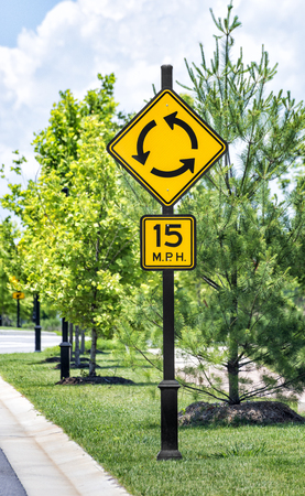 Vertical shot of a roundabout traffic sign with speed limit sign below in an upscale industrial...