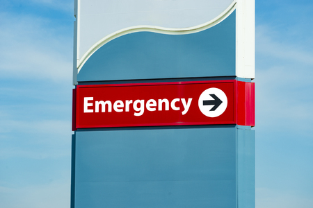 Horizontal close-up shot of a hospital emergency room sign.  Cloudy sky background.