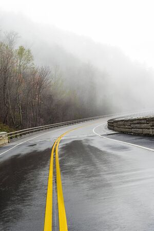 Horizontal shot of a wet curving Smoky Mountain road disappearing into fog with copy space.