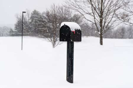 Horizontal shot of a black mailbox on a pole on a snowy day.の写真素材