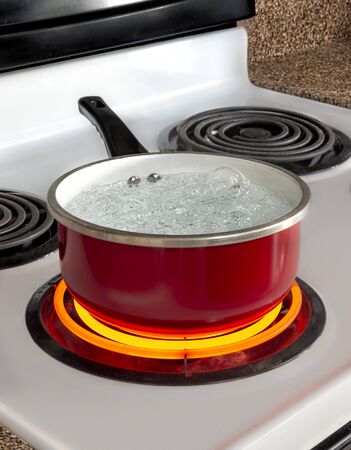 Vertical shot of a red pan of boiling water on top of a stove with the burner turned to high.の写真素材