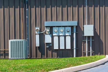 Horizontal shot of an air conditioner and electric meters outside of an office complex.