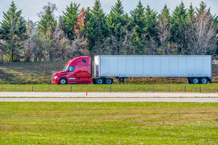 Horizontal shot of a red tractor trailer traveling on a lonely late summer highway.                 ...