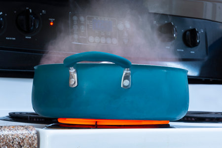 Horizontal shot of a blue pot on a stove top on a red hot burner with steam rising out of it.
