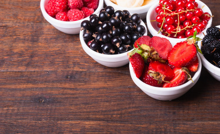 row of wild berries in bowls on wooden backgroundの写真素材