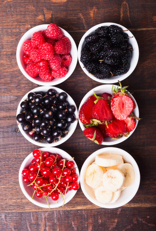 row of wild berries in bowls on wooden backgroundの写真素材