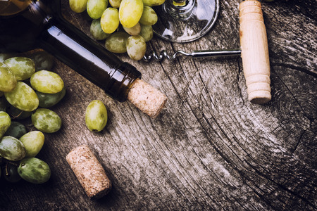 Bottle of white wine, glass, grape and corks on old wooden backgroundの写真素材