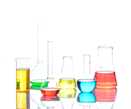 Laboratory glassware with colored liquids over reflective table over whiteの写真素材