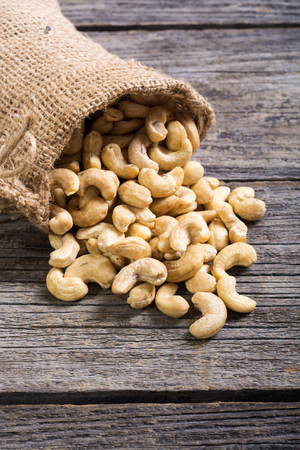 Cashew nuts in burlap bag on wooden background . Healthy foodの写真素材