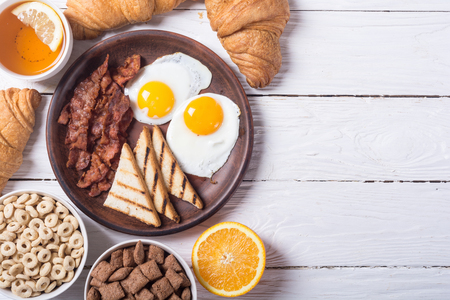 Breakfast with eggs , bacon , croissants , cereals and lemon teaの写真素材