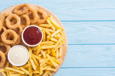 French fries and onion rings with sauces on wooden boardの写真素材