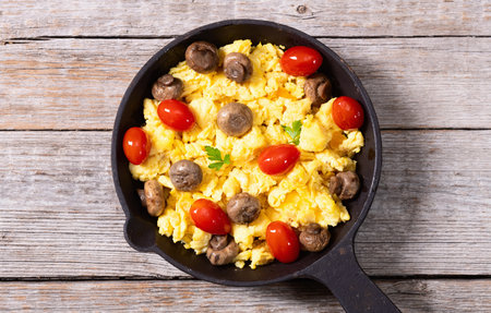 Healthy vegetarian breakfast. Scrambled eggs in pan with cherry tomatoes and parsley. Top viewの写真素材