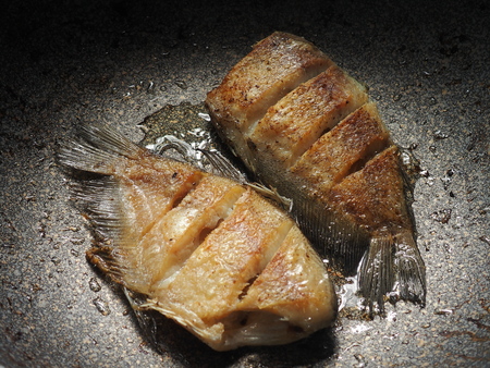 oily fried fish in dark pan not good for calories controlの写真素材