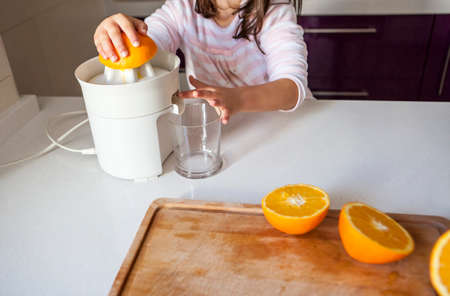 Little girl squeezing orange juice with a juicer in the kitchenの写真素材