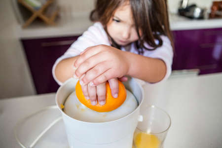 Little girl squeezing orange juice with a juicer in the kitchenの写真素材