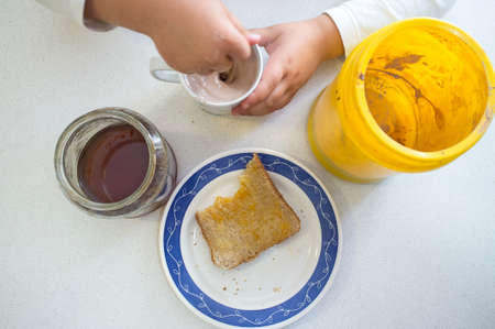 Little girl preparing her afternoon snack. Chocolate powder with milk, honey and toastの写真素材
