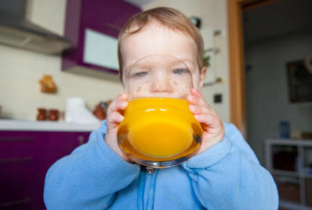 Baby boy drinking a big glass of orange juice fresh made. Education on healthy nutrition for children conceptの写真素材