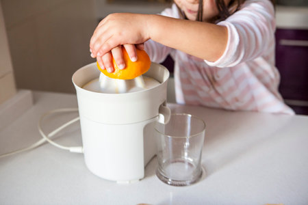 Little girl squeezing orange juice with a juicer in the kitchenの写真素材