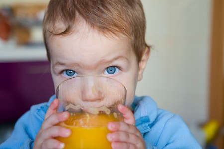 Baby boy drinking a big glass of orange juice fresh made. Education on healthy nutrition for children conceptの写真素材